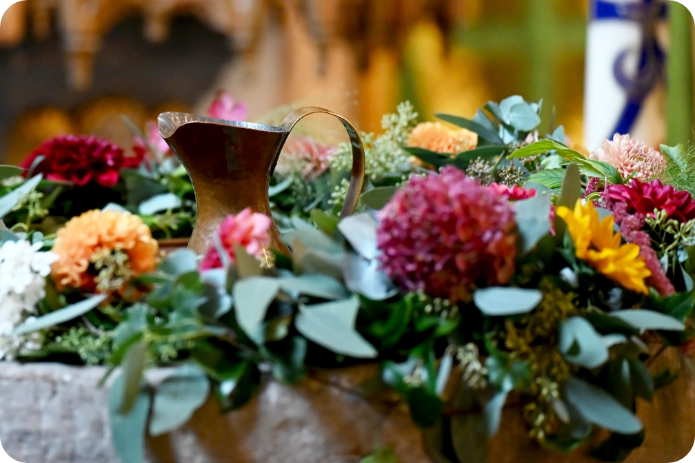 Eine Taufkanne in einem großen Blumengesteck.